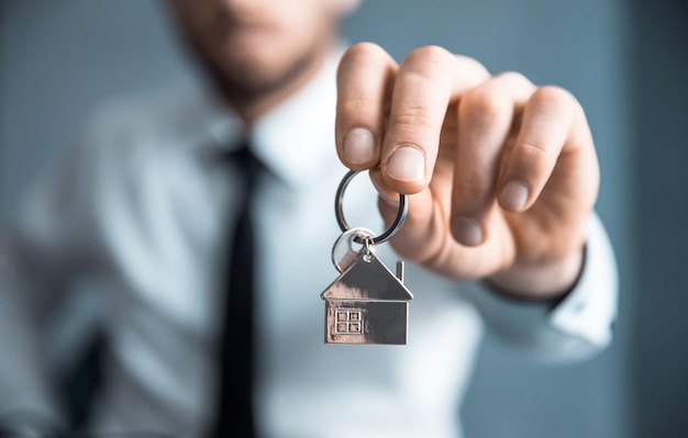 Chave da casa da mão do jovem empresário no fundo cinza xa