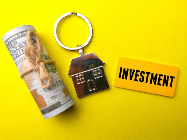 Chaveiro Banknotehouse e placa de madeira com a palavra INVESTIMENTO em um fundo amarelo Conceito de negócio