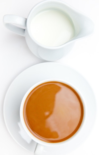 Chávena de café branca ao lado de uma panela de leite