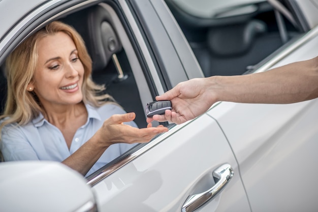 Foto chaves do carro. mulher loira sorridente pegando as chaves do carro e parecendo satisfeita