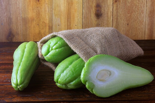 Chayote crudo, fresco y orgánico, entero y cortado en una bolsa rústica en mesa de madera