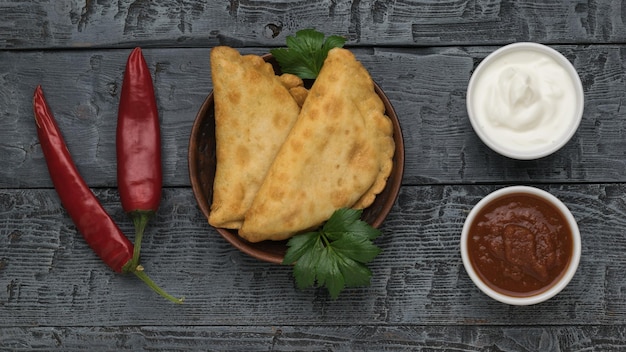 Chebureks fritos dos tazas con salsa y pimiento rojo sobre una mesa de madera