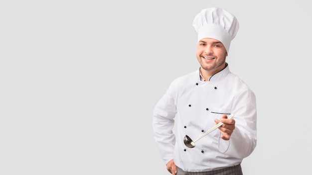 Cheerful Chef Man sosteniendo la cuchara de pie sobre el fondo blanco Panorama