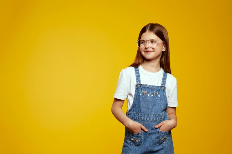 Cheerful child in stylish denim overalls with hands in pockets looking confidently to the free space