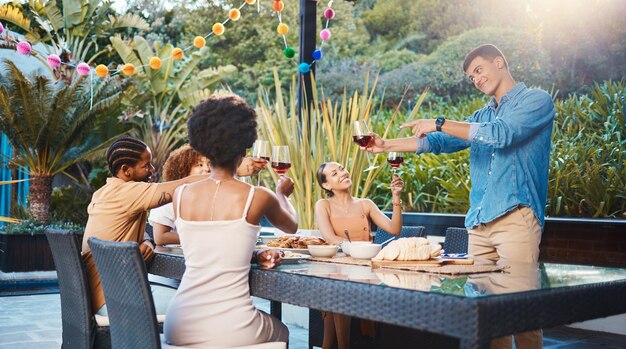 Cheers comemorar e amigos no jantar no jardim na festa e diversidade comida e vinho em evento ao ar livre brinde de vidro homens e mulheres na mesa pessoas divertidas com bebidas ao pôr do sol no quintal juntos