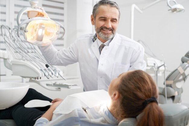 Cheerul dentista sorrindo, olhando para o paciente.