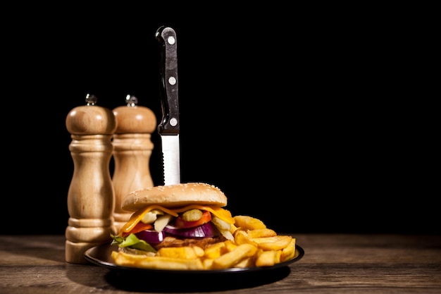 Cheesburgers caseros clásicos sobre placa negra y fondo junto a papas fritas. Comida rápida. Refrigerio poco saludable