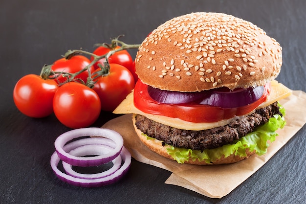 Cheeseburger caseiro com rissóis de carne, salada fresca, tomate e cebola em pãezinhos de marinhas, servido na mesa de ardósia preta.