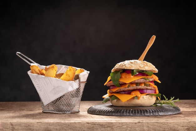 Cheeseburger com batatas em uma mesa de madeira e uma parede escura