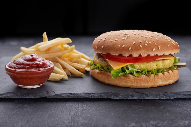 Cheeseburger com carne, batatas e molho, em uma pedra preta