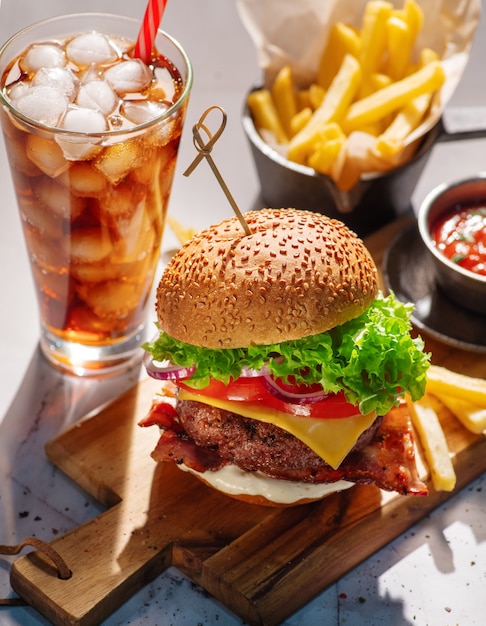 Cheeseburger com carne, queijo, tomate, cebola e alface e um copo de refrigerante gelado e batatas fritas.