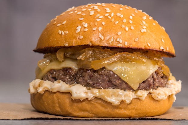 Cheeseburger com molho e cebola caramelizada em papel pardo em fundo cinza