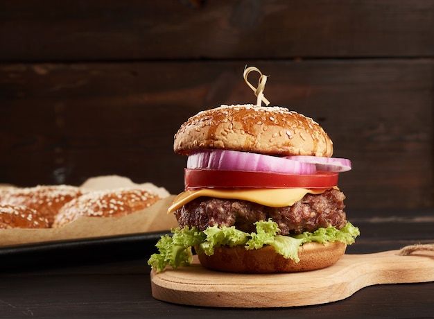 Cheeseburger com tomate, costeleta de churrasco e pão de gergelim em uma velha tábua de madeira