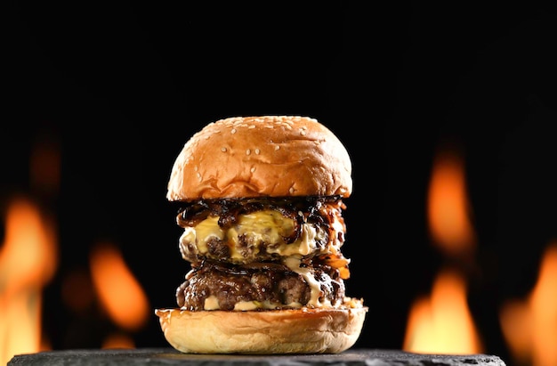 Cheeseburger duplo de carne com cebola caramelizada na chapa preta sobre fundo em chamas