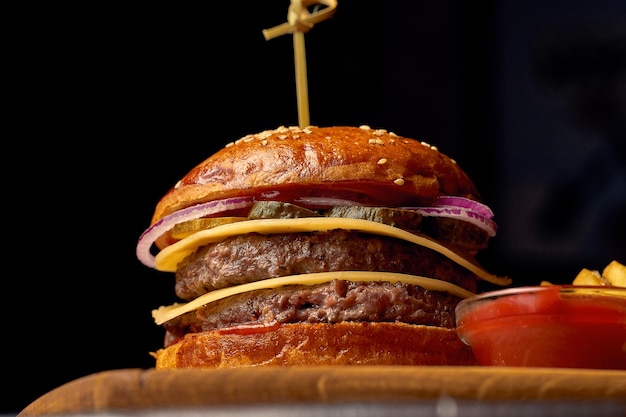 Cheeseburger duplo de fast-food americano em uma placa de madeira. Fundo de madeira escuro. Foco seletivo.