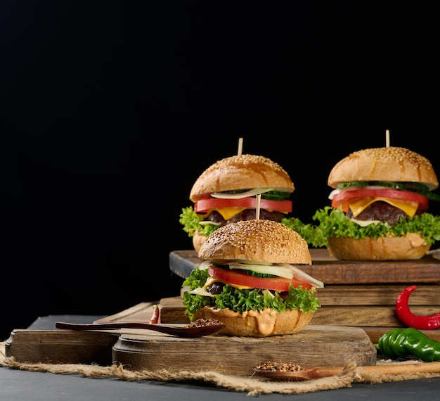Cheeseburger mit gegrilltem Rindfleischpatty, Cheddar-Käse, Tomate und Salat auf einem Holzbrett, schwarzer Hintergrund