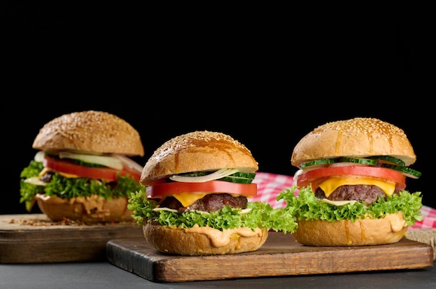 Cheeseburger mit gegrilltem Rindfleischpatty, Cheddar-Käse, Tomate und Salat auf einem Holzbrett, schwarzer Hintergrund