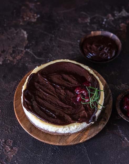 Cheesecake cremoso com calda de chocolate e cereja decorado com alecrim