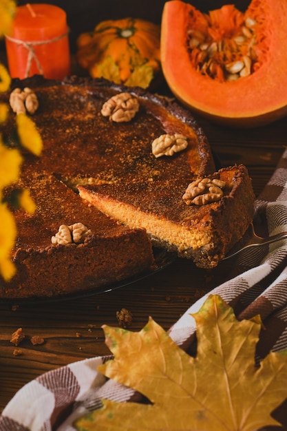 Cheesecake de abóbora caseiro fresco com chantilly e nozes, com ingredientes e flores de outono na mesa de madeira