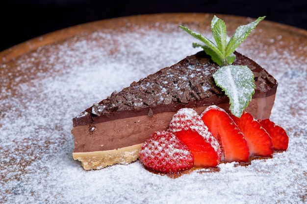 Cheesecake de chocolate com morangos e açúcar de confeiteiro em uma placa de madeira