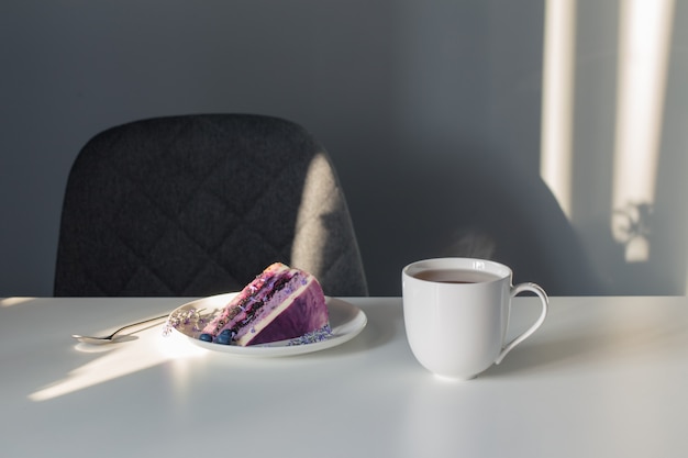 Cheesecake de mirtilo e lavanda no prato e xícara de chá na mesa branca