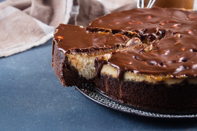 Cheesecake Snickers com caramelo, Nougat e amendoim Layered bolo na backgro azul de concreto