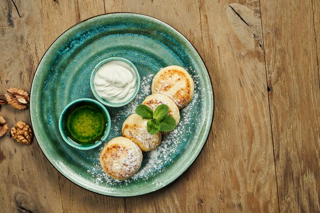 Cheesecakes caseiros ou Syrniki com geléia, frutas frescas e creme de leite na placa cerâmica. Cozinha ucraniana. Comida de café da manhã. Superfície de madeira