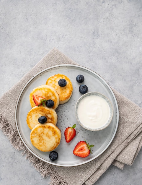 Cheesecakes ou queijo cottage ou syrniki com blerries frescas e creme azedo em um fundo cinza o conceito de café da manhã saudável e delicioso vista superior e espaço de cópia