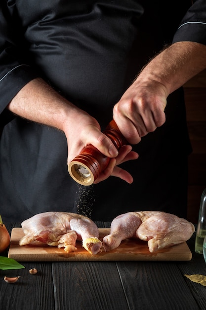 chef adiciona pimenta nas pernas de frango grelhadas em branco com coxa de frango crua na cozinha de um restaurante ou café