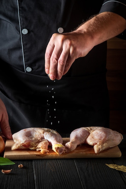 chef adiciona sal à preparação de coxas de frango cru para grelhar com coxa de frango em um restaurante de cozinha