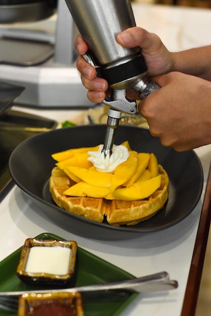 Chef adicionando creme fresco em manga fatiada em waffles belgas assados com espremedor de creme