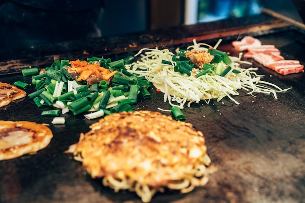 chef adicionando vegetais de cebola verde na culinária okonomiyaki no restaurante local na panela teppanyaki. deliciosa comida de rua de panqueca de estilo japonês saborosa na chapa de ferro quente.