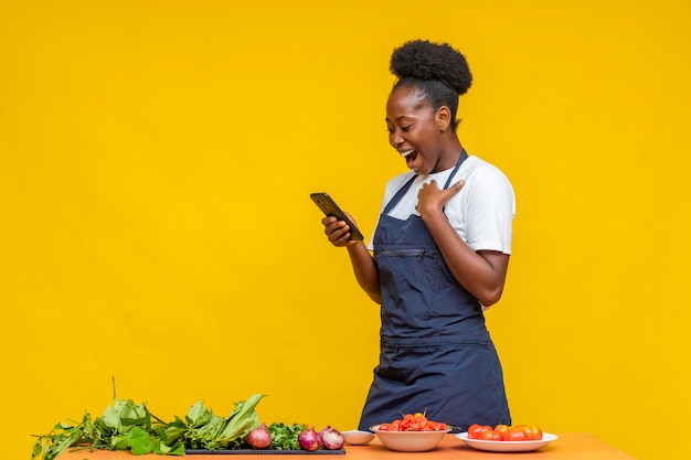 Chef africana femenina mirando con entusiasmo a su teléfono