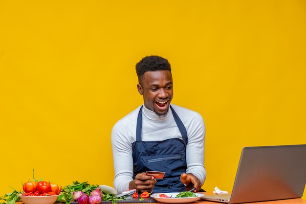 Chef africano empolgado olhando para seu laptop enquanto segura um cartão de crédito