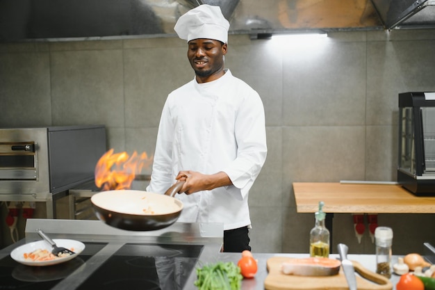 Chef afroamericano prepara la comida con fuego en el restaurante de la cocina Chef con wok en la cocina