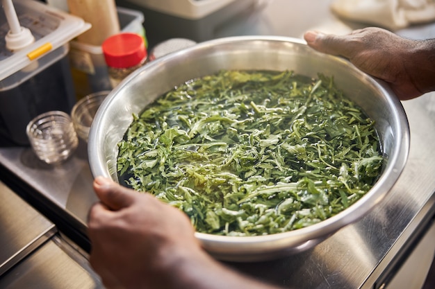 Chef afroamericano sosteniendo un tazón con vegetación y agua en la mesa