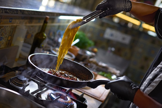 El chef agrega espagueti frito en una sartén los tomates y las ostras,