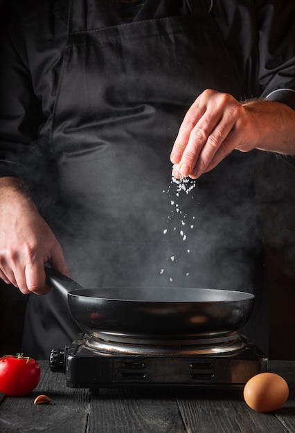 El chef agrega sal mientras cocina los huevos en una sartén.