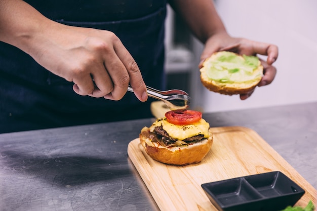 Chef agregue una rodaja de tomate para hacer una hamburguesa de carne en placa de madera