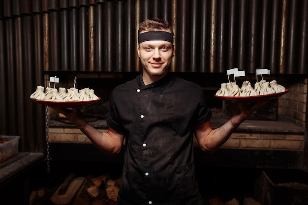 Chef alegre posando com uma porção de cozinha tradicional nacional georgiana Khinkali Processo de cozimento Conceito de comida de cozinha