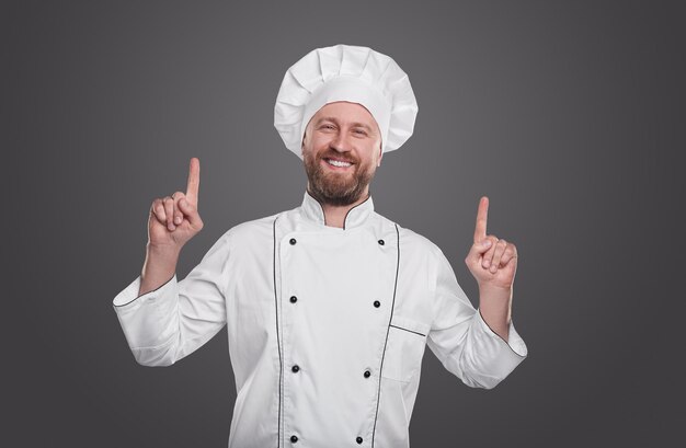 Chef alegre en uniforme apuntando hacia arriba