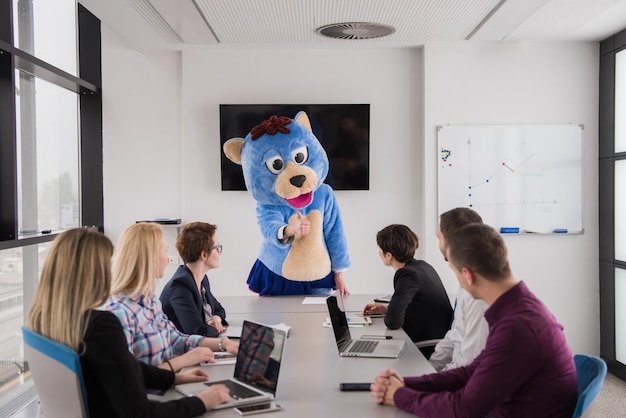 Chef als Teddybär verkleidet, der Spaß mit Geschäftsleuten in modernen Firmenbüros hat