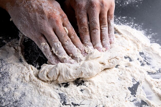 El chef amasa la masa sobre un fondo oscuro, la mesa está cubierta de harina