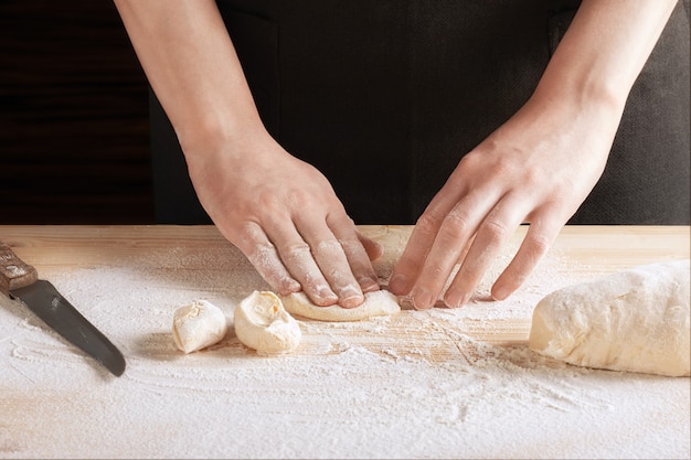 Chef, amassar uma fatia de massa sobre uma mesa de madeira polvilhada com farinha