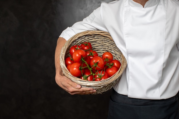 Chef anónimo con canasta con tomates maduros