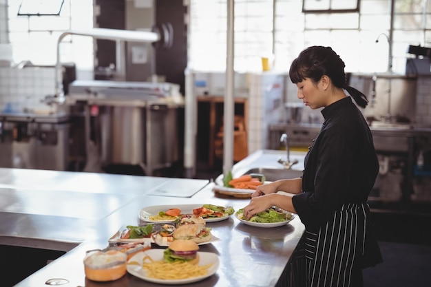 Chef asiática preparando ensalada en una cocina comercial con comida platada y espacio de copia de mesa de preparación
