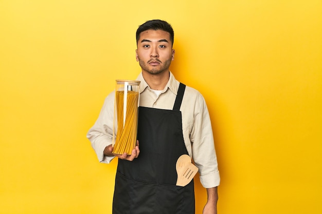 Chef asiático segurando um frasco de espaguete em um fundo de estúdio amarelo