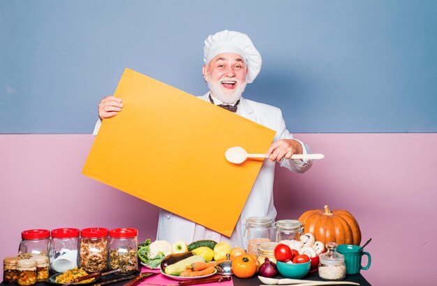 El chef asombrado señala la cuchara en el menú en blanco del tablero Anuncio de la profesión de cocina y concepto de personas Tabla negra del menú para la publicidad