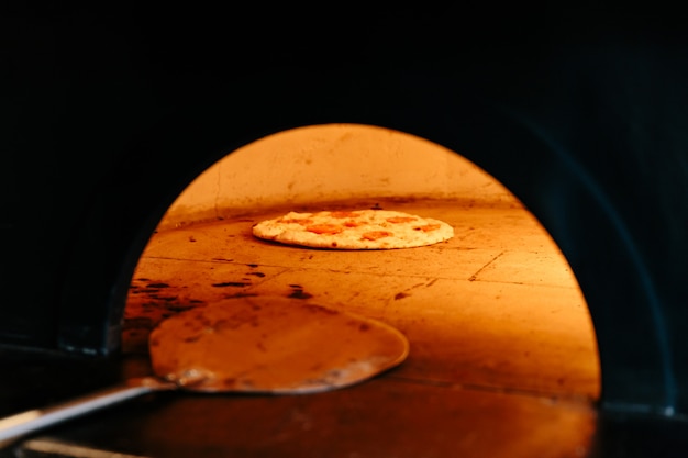 Chef Baking Caprese Bianca Pizza innerhalb des hölzernen brennenden Pizzaofens.