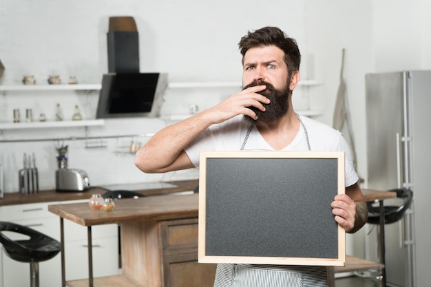 El chef barbudo brutal y serio tiene una tabla en blanco para la búsqueda de trabajo en el espacio de copia